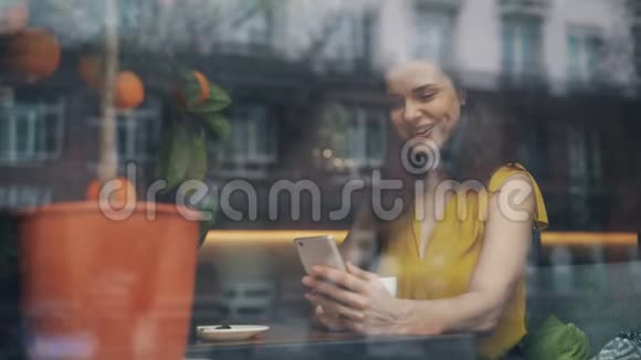 在咖啡馆里一个微笑的年轻女子在看智能手机屏幕视频的预览图