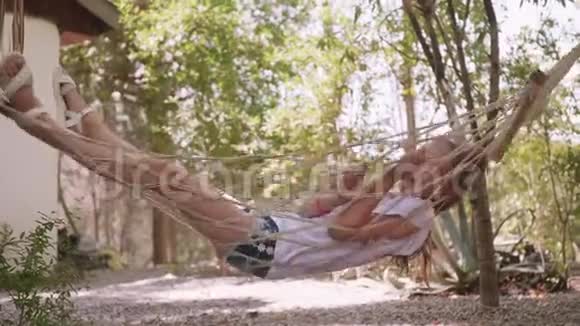 放轻松的女孩在暑假在吊床上摇摆少女在树上的夏日花园的吊床上放松视频的预览图
