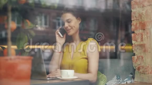 有魅力的学生在现代咖啡馆用手提电脑工作用手机说话视频的预览图