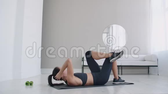 布鲁内特躺在地板上做腹肌肌肉锻炼把身体抬到膝盖上视频的预览图