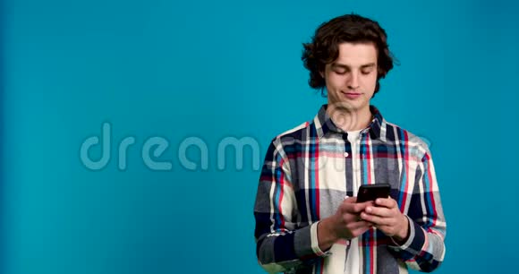 聚焦男人在智能手机上打字微笑和闪烁在蓝色背景上的正面视图视频的预览图