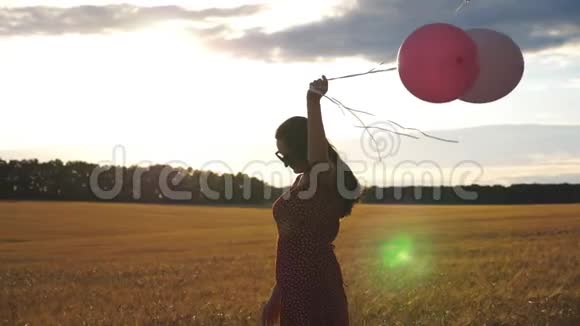 美丽的女人穿着红色的裙子穿过麦田手里拿着气球棕色头发的快乐少女视频的预览图