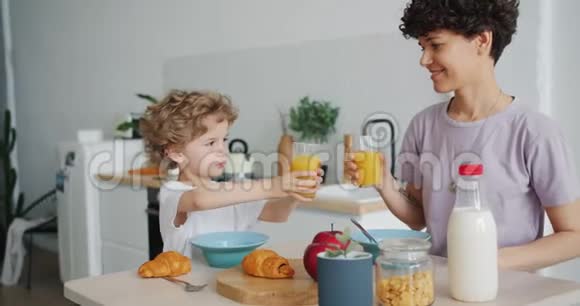 母亲和儿子在家里用橙汁碰杯吃羊角面包视频的预览图