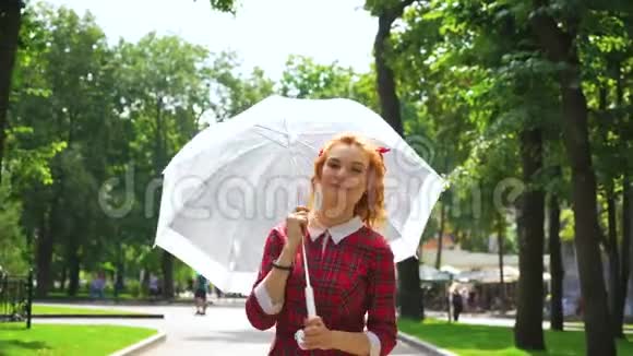 公园里穿着红裙子打着白伞的红发女孩微笑视频的预览图