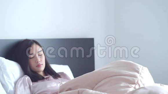 美丽的亚洲女人穿着性感的粉红色睡衣从白色的卧室醒来她看着相机微笑着视频的预览图
