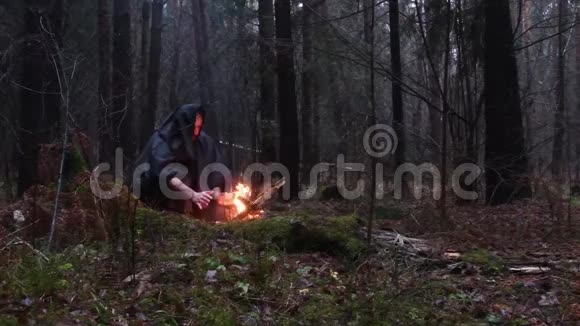 一个穿着黑色长袍的老和尚正在黑暗的秋林中用火取暖视频的预览图