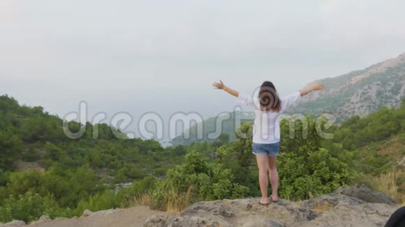 旅游妇女站在山边伸展双手旅行妇女举起双手欣赏青山绿水视频的预览图