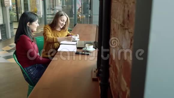 两个年轻的女人在咖啡馆里讨论一个新项目并喝咖啡视频的预览图