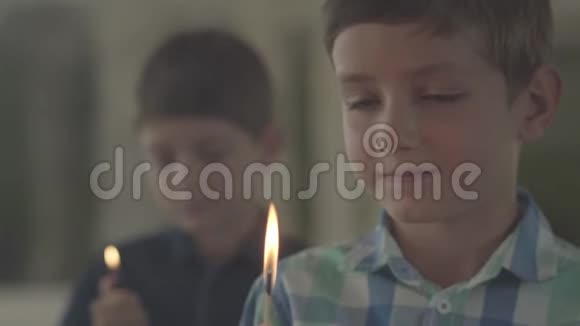 两个可爱的兄弟在黑暗的烟雾弥漫的房间里带着火一个男孩在背景中点燃打火机另一个男孩在背景中点燃火柴视频的预览图