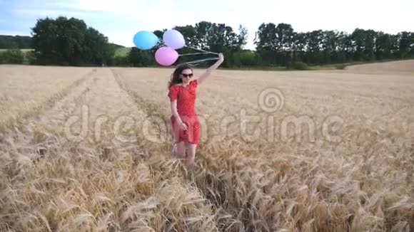 年轻的微笑的女人穿着红色的衣服手里拿着气球在金色的麦田里慢跑可爱的快乐女孩视频的预览图