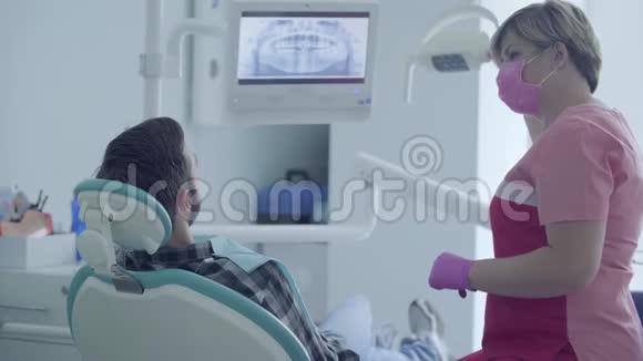 戴口罩和手套的牙医在现代牙科诊所使用医疗工具检查病人的口腔视频的预览图