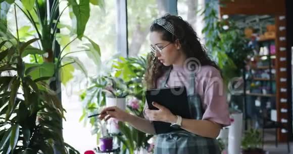 漂亮的花店老板在工作中清点植物和使用平板电脑视频的预览图