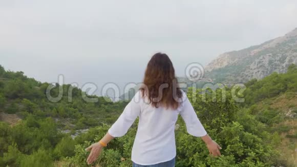 在雾山欣赏晨景的旅行妇女旅游妇女在山边伸展双手女孩视频的预览图