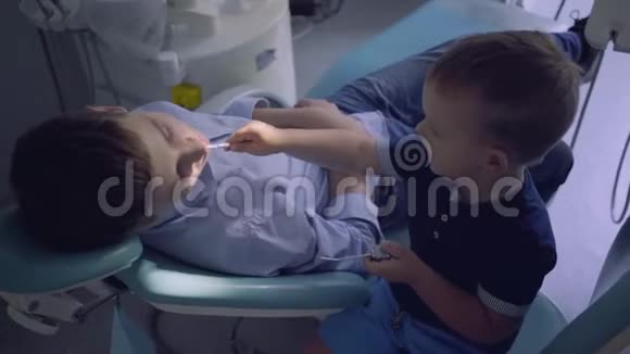 小男孩扮演医生十几岁的男孩坐在牙医办公室的椅子上孩子检查男孩的牙齿孩子视频的预览图