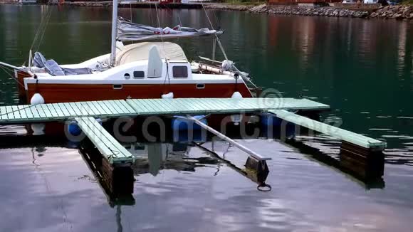 木船双体帆船系在浅绿色的码头岩石上轻轻地系在岩石海岸附近的平静水域上视频的预览图