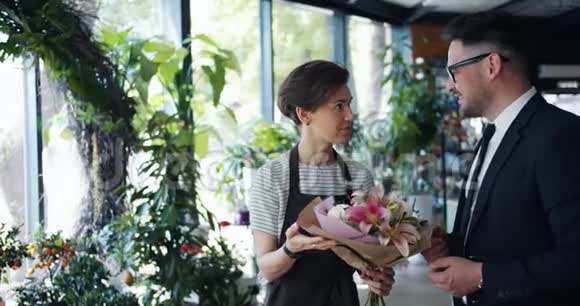 花店里拿着花束的花商和顾客说话的慢动作视频的预览图