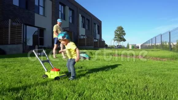 父亲用割草机剪草坪儿子玩玩具割草机万向节运动视频的预览图