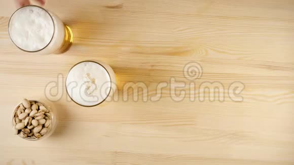 新鲜啤酒手从背景的木桌上拿一杯啤酒放在其他杯子和碟子旁边视频的预览图