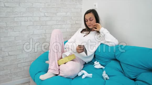 生病的年轻女子坐在沙发上在家里用纸纸吹鼻子视频的预览图