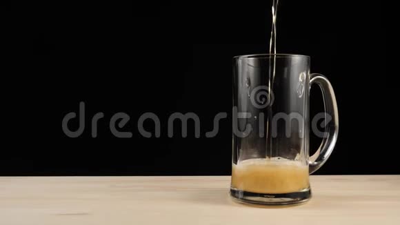 新鲜啤酒手在啤酒杯中将美味的工艺啤酒从棕色的瓶子倒入黑色背景的木桌中视频的预览图