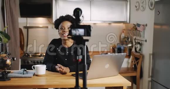 快乐年轻的黑人旅行博主女人在家里用相机制作新的vlog视频笑着说着慢动作视频的预览图