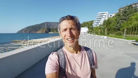 迷人的微笑男博主在阳光明媚的日子在海湾拍视频自拍视频的预览图