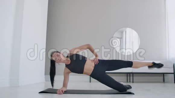 公寓里的黑发女人做一个运动外侧木板站在她的膝盖上抬起她的腿健身视频的预览图