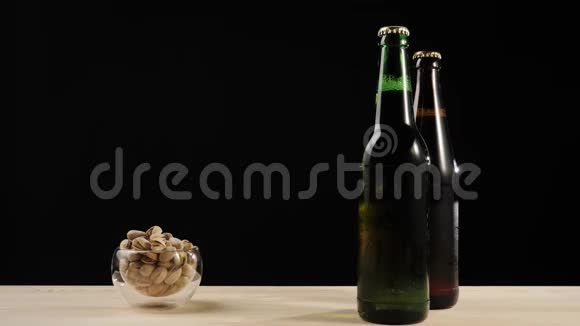 新鲜啤酒在木桌上用装有美味工艺啤酒的绿色和棕色小瓶旁的开心果碟递出去视频的预览图