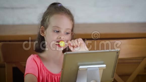 美丽的小女孩吃冰淇淋看平板电脑上的卡通视频的预览图