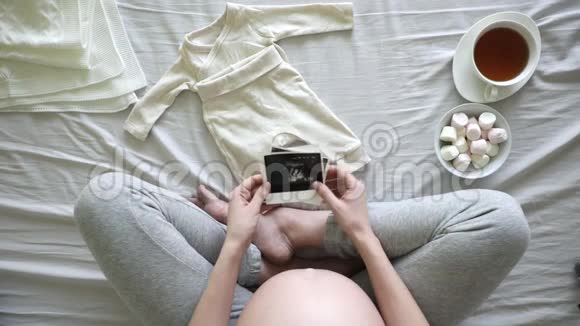孕妇在床上准备婴儿衣服怀孕和分娩概念的俯视图视频的预览图