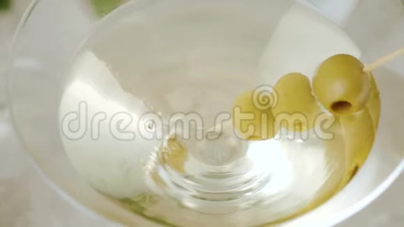 豪华马提尼手拿三个绿色橄榄在鸡尾酒棒从玻璃与马提尼装饰在桌子上视频的预览图