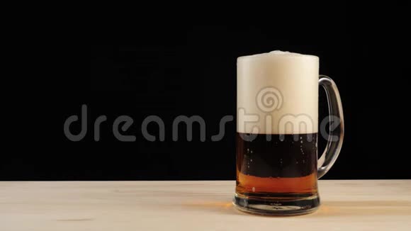 新鲜啤酒手从黑色背景的木桌上拿着一杯美味的工艺啤酒在啤酒杯里冷鲜啤酒视频的预览图