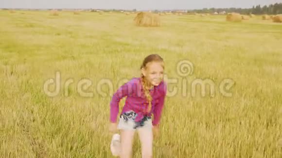 在黄色草地上跑向干草堆的快乐女孩少女在收割场的干草堆上攀爬嬉戏视频的预览图