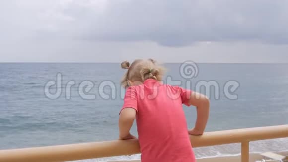一个小女孩站在水边俯瞰大海靠在篱笆上视频的预览图