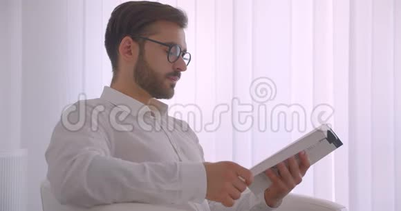 特写侧景照片一位戴眼镜的英俊的白种人成年商人正坐在扶手椅上看书视频的预览图