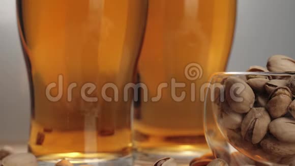 新鲜啤酒一些开心果倒在碟子里靠近两杯啤酒倒在白色背景的木桌上视频的预览图