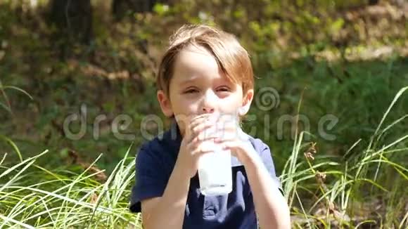 大自然中一个快乐的孩子喜欢从一个透明的杯子里慢慢地喝奶制品中的kefi视频的预览图