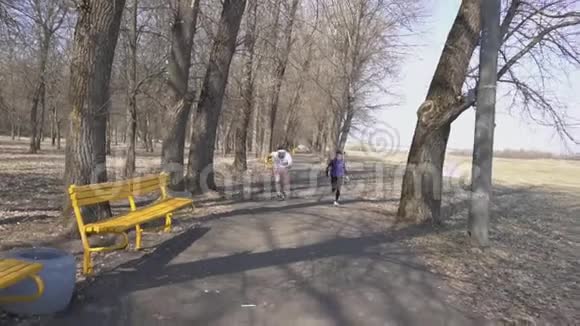 年轻的大胡子男教练和苗条的女教练在公园里赛跑健康的生活方式春天慢动作视频的预览图