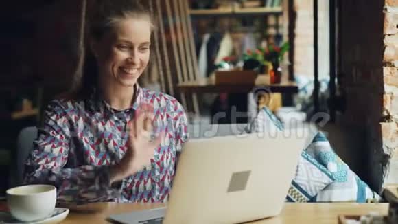 开朗的年轻女士与笔记本电脑交流在咖啡馆里微笑交谈视频的预览图