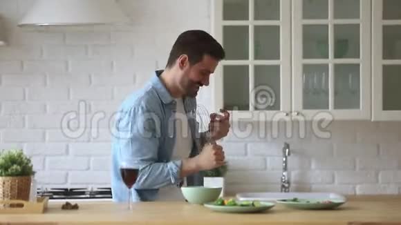 有趣的男人在厨房里用麦克风唱歌跳舞做饭视频的预览图