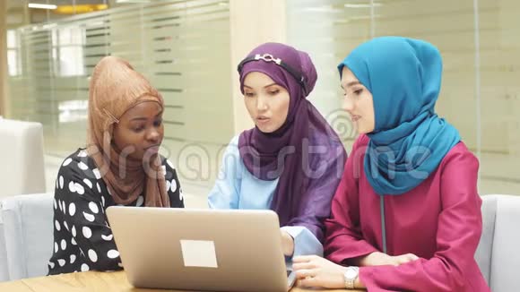 一群多民族的穆斯林商业女性坐在咖啡馆里用笔记本电脑在线购买视频的预览图