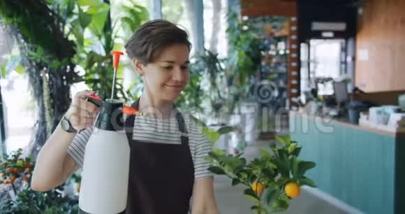 美丽的女士花店在花盆里浇花手里拿着喷头微笑视频的预览图
