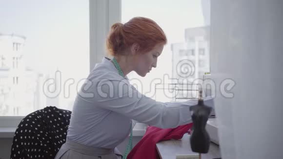 专业漂亮的红发女人在车间的桌子上缝衣服裁缝工作勤奋细心业余爱好视频的预览图