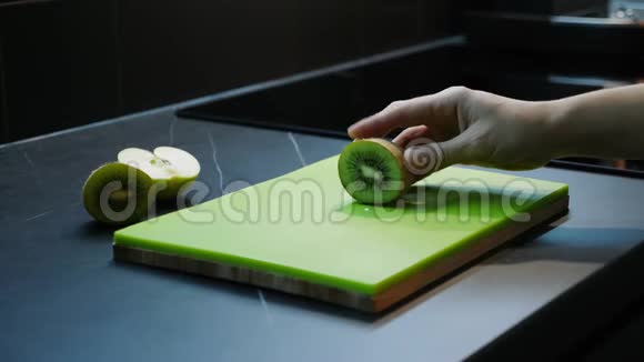 切猕猴桃的雌性年轻女子在木塑砧板上用刀切绿猕猴桃侧视特写厨房和食品视频的预览图