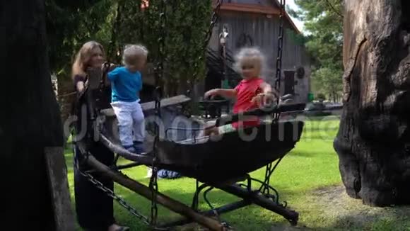 年轻漂亮的母亲带着孩子在公园的木马车上荡秋千视频的预览图