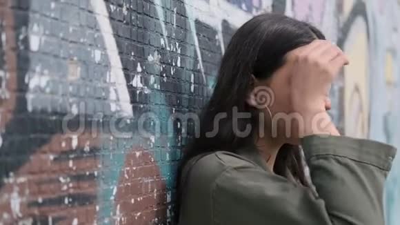 年轻漂亮体贴深褐色头发的女孩站在墙边涂鸦手伸进头发视频的预览图