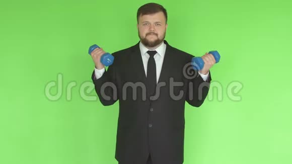 年轻的白种人留胡子的男商人穿着黑色西装在健身房做运动用哑铃摇动他的二头肌健康视频的预览图