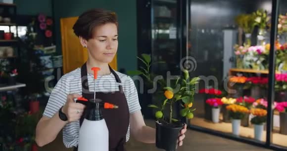 兴高采烈的年轻花匠在花店用喷雾机浇花享受工作视频的预览图