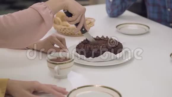 在桌子上特写一个美味的巧克力蛋糕女性白种人的手把美味的甜点切成四块家庭视频的预览图