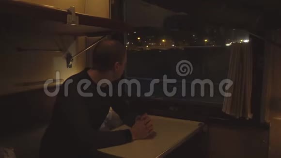 一位男性乘客坐在火车车厢里看着窗外晚上乘火车旅行视频的预览图